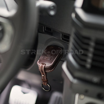 Brown leather keychain with a logo on a car dashboard, featuring 'STREK OFFROAD' branding.