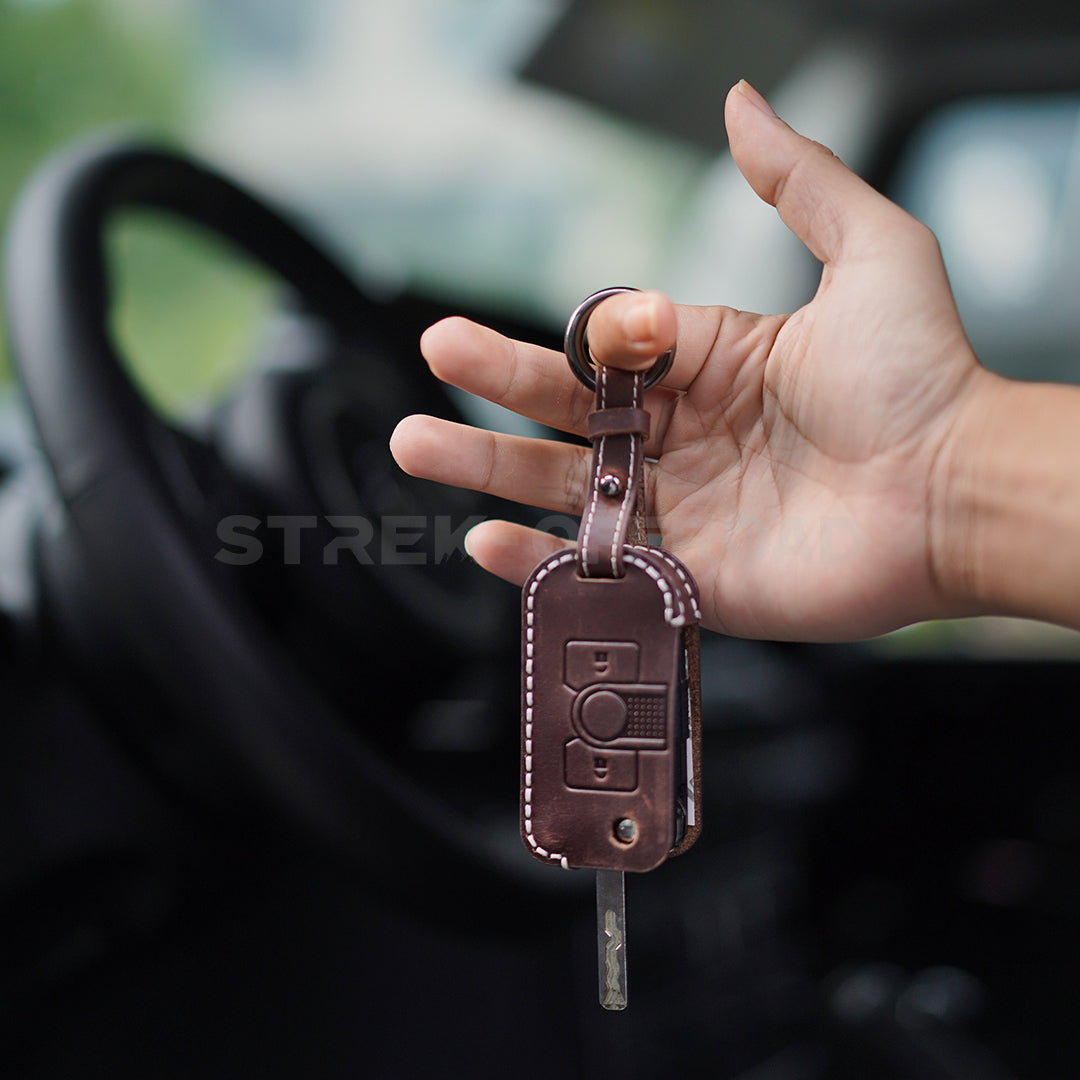 Hand holding a leather car key fob with a blurred car interior background