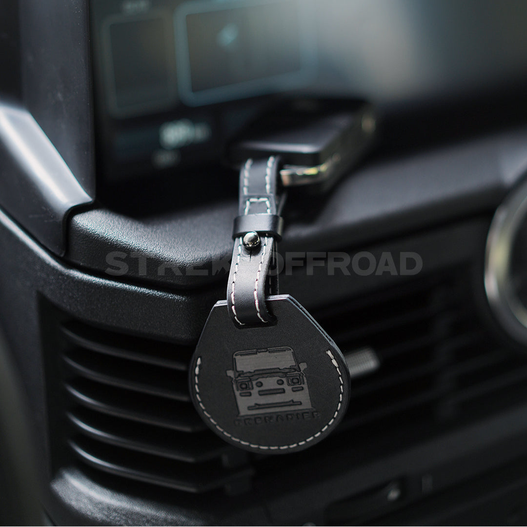 Black leather keychain with a car emblem attached to a car's air vent.