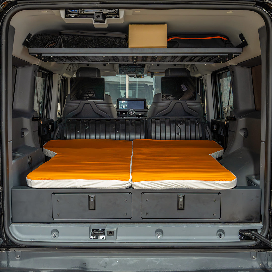 Straight-on rear trunk view of the orange sleeping mattress fitted flush on the INEOS Grenadier drawer system.
