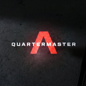 Illuminated red chevron graphic and white Quartermaster text projected on the ground from the LED puddle light.