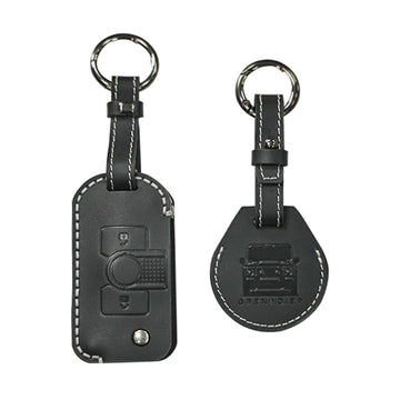 STREK Off Road black genuine leather keychain cover and matching AirTag case set compatible with INEOS Grenadier fob, featuring white contrast stitching on a white background.