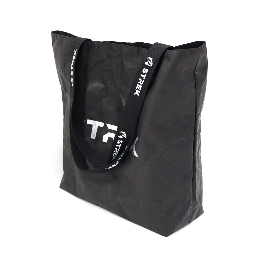 STREK Overland Tyvek Utility Tote Bag shown at an angled standing view with black crinkle-textured Tyvek material and branded handles.