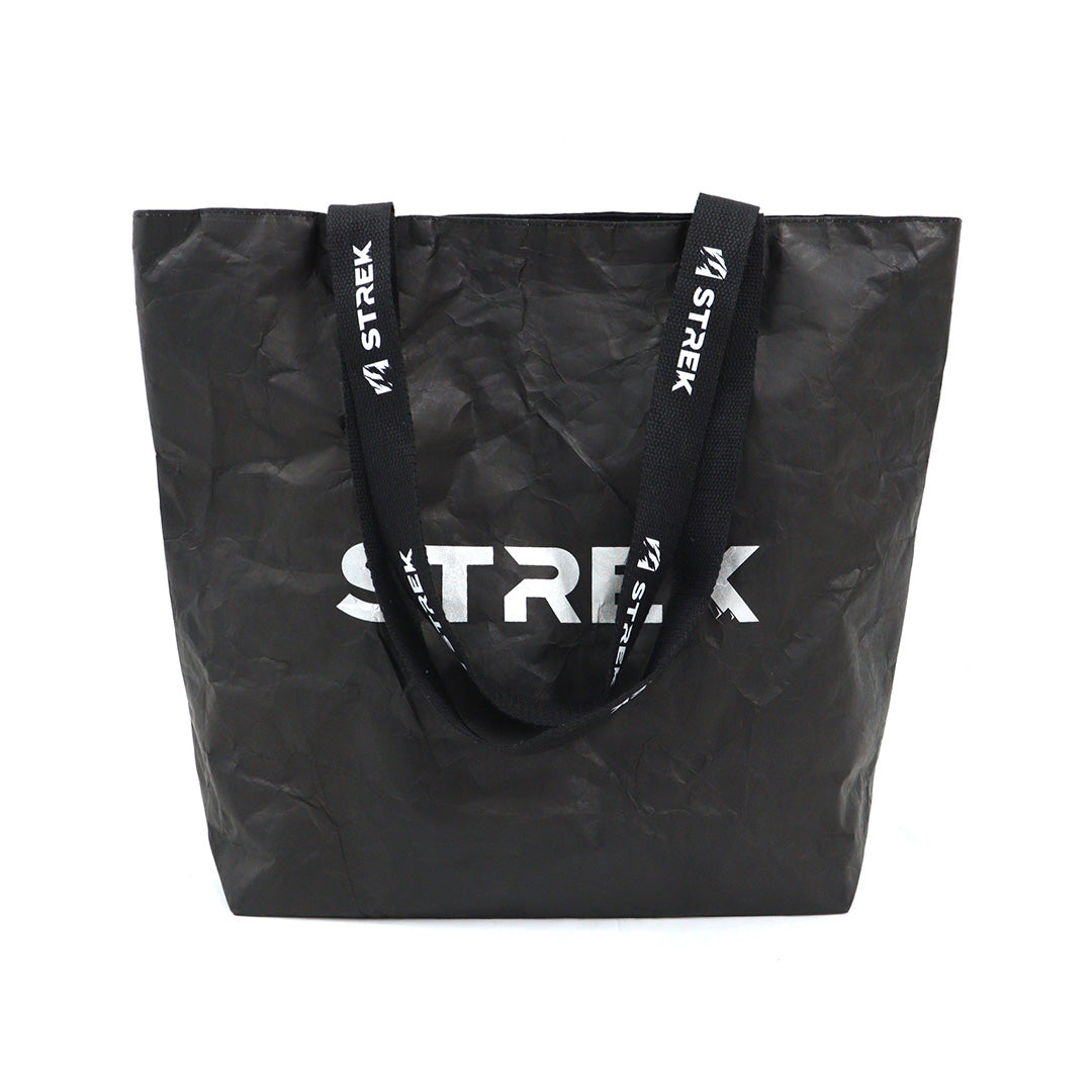 Front view of the STREK Overland Tyvek Utility Tote Bag with black crinkle-textured body, white STREK logo, and branded shoulder handles.