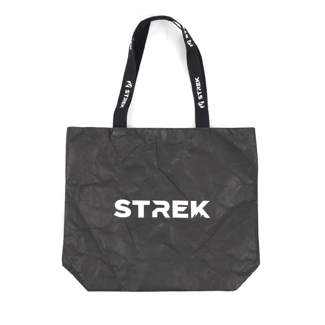 Full front product view of the STREK Overland Tyvek Utility Tote Bag with STREK logo on a black crinkle-textured tote body.