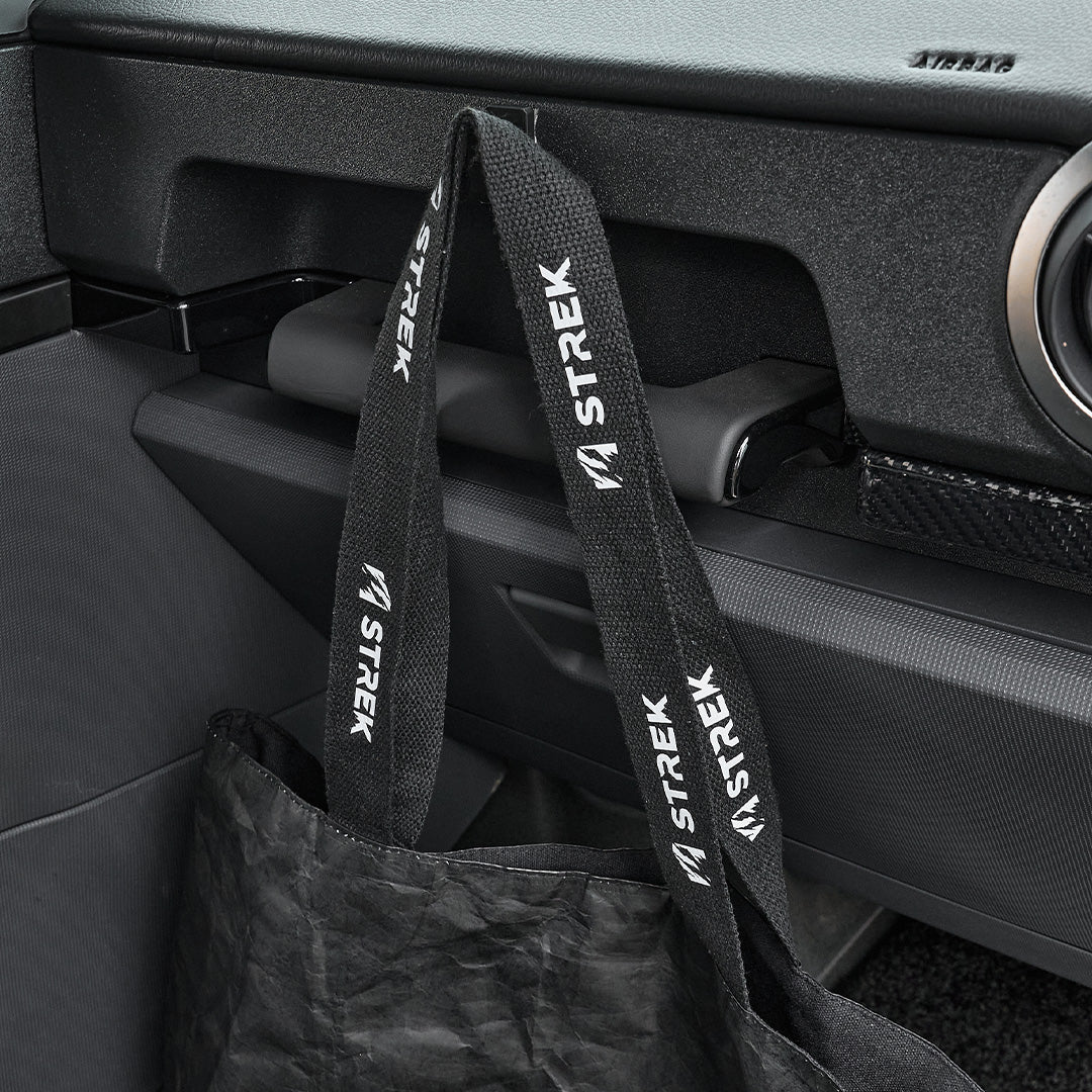 Close-up of the STREK Overland Tyvek Utility Tote Bag showing the branded black woven handles inside an INEOS Grenadier interior.